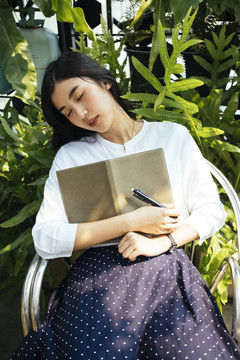在花园里，一个亚洲女人拿着一本书睡在椅子上。