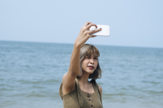 短发女孩站在沙滩上，坐在海边的岩石上自拍。