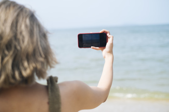 短发女孩在旅行中拍海上照片时，智能手机屏幕上的一张剪短的照片，肩上的照片。