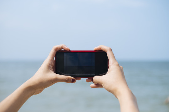 短发女孩在旅行中拍摄大海照片时，智能手机屏幕上的一张裁剪图像。