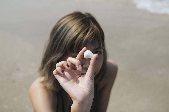 穿着短牛仔裤的短发女孩坐在海边的海滩上收集贝壳。