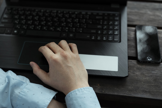 木桌上黑色笔记本电脑上男人手的剪影。