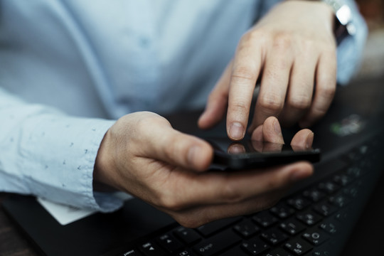 一个自由职业者手上的智能手机在笔记本电脑附近的剪短图像。