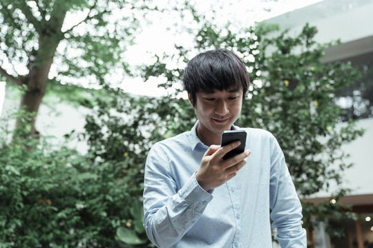 一个穿着蓝色衬衫的男人站在咖啡馆的花园里，手里拿着手机。