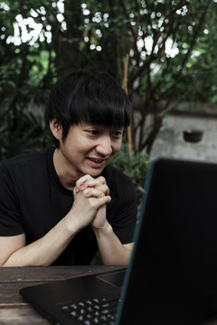 一个穿着黑色t恤的男人在花园里用笔记本电脑观看一场激动人心的足球赛。