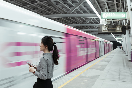 一名泰国妇女手持智能手机，晚上等火车回家——复印空间。