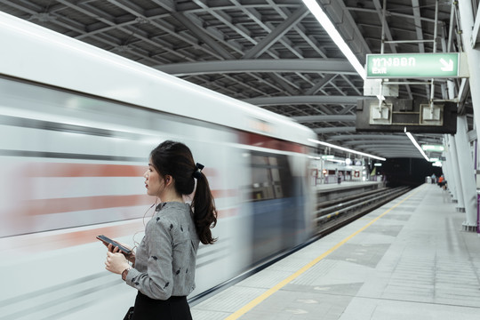 一名泰国妇女手持智能手机，晚上等火车回家——复印空间。