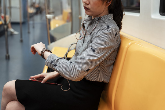 亚泰妇女在看时间，坐在火车里的黄色椅子上，用耳机听音乐。
