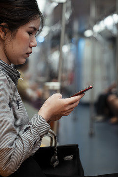 亚泰妇女在火车上使用智能手机的侧视图。