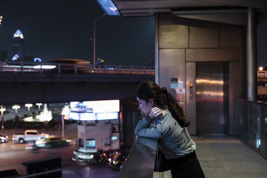 站在天桥上的亚泰妇女在夜间看路的侧视图-复印空间