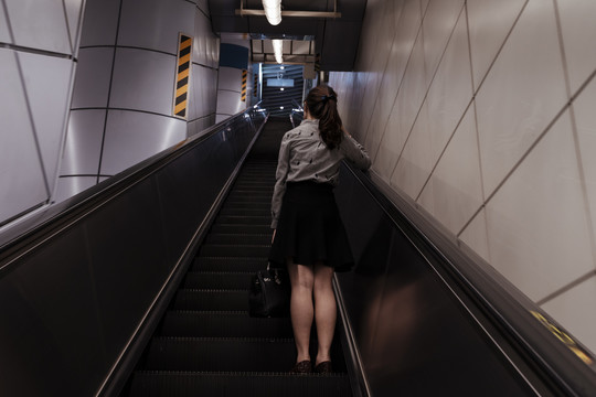 在地铁站使用自动扶梯上楼的妇女。