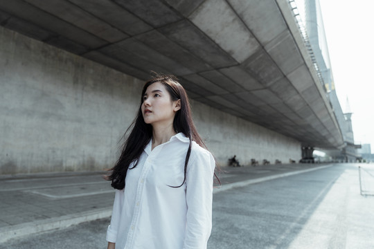 夏天，穿白衬衫的黑长发女人沿着桥下的主线走着。