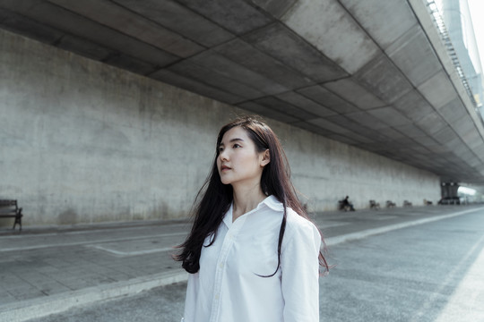 穿着白衬衫的黑色长发女子在夏天沿着桥下的领路走着，头发边缘泛着亮光。