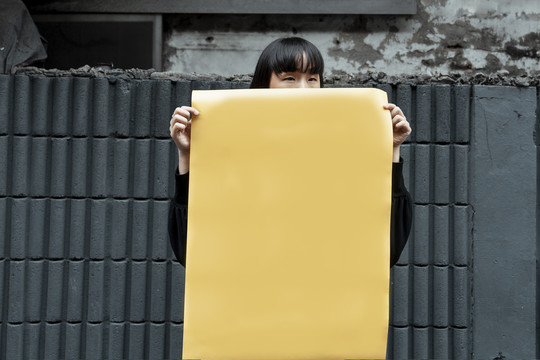 年轻的泰国亚裔女子，深色短发，手里拿着黄色的空纸。实体模型。