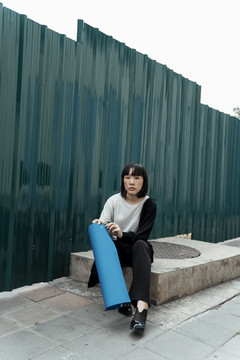 年轻的泰国亚裔女子深色短发，蓝色墙纸坐在街上。