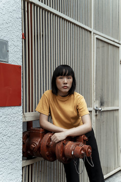 年轻的泰国亚裔女子深色短发穿着橙色衬衫站在街上。