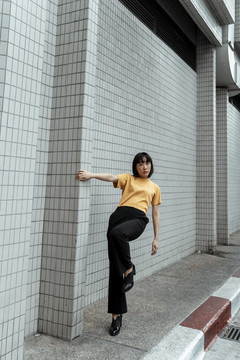 年轻的泰国亚裔女子深色短发穿着橙色衬衫，单腿站在街上。运动员生涯。