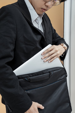 穿黑色西装的商人从手提包里拿出白色的电脑笔记本。