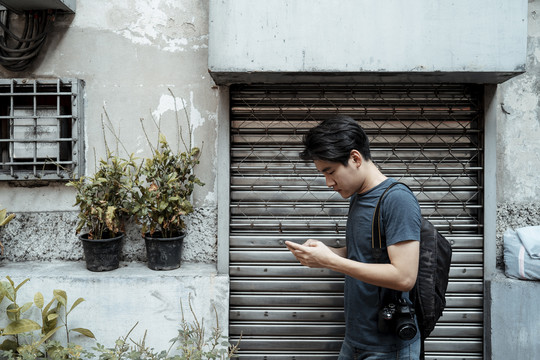 年轻英俊的亚洲摄影师用智能手机在市区散步。