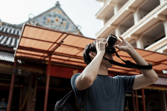 年轻英俊的亚洲摄影师手持相机在中国寺庙旅行。