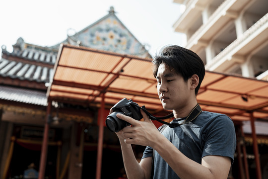 年轻英俊的亚洲摄影师手持相机在中国寺庙旅行。