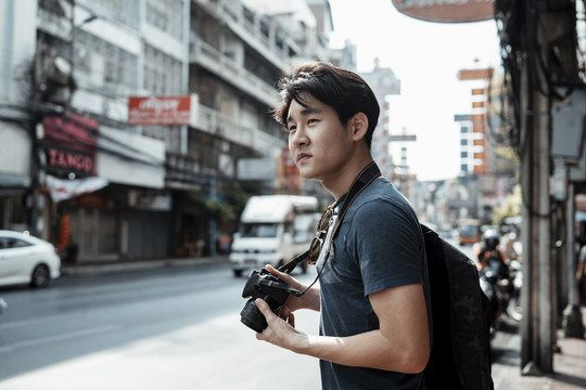 年轻英俊的亚洲摄影师走在街上用相机拍照。街头摄影。