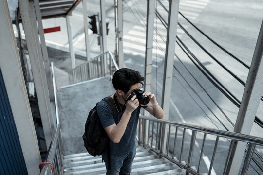 年轻英俊的亚洲摄影师在马路上的楼梯上拍照。