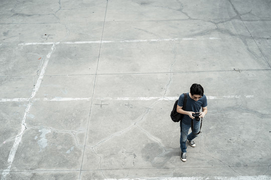 顶视图-年轻英俊的亚洲摄影师男子走在水泥地面上的城市-复制空间。