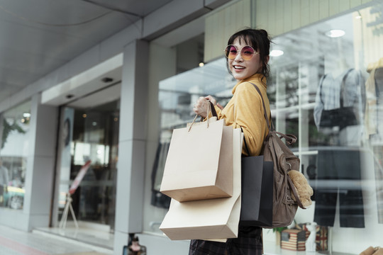 时尚达人快活的亚洲女人喜欢穿着黄色毛衣戴着时尚眼镜在商店外的大街上逛街。