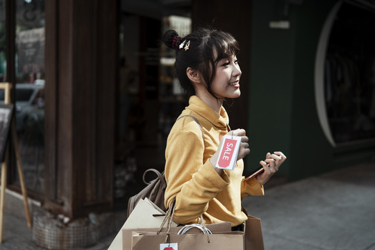 侧视亚洲女人穿着黄色毛衣拿着购物纸袋许多价格标签。