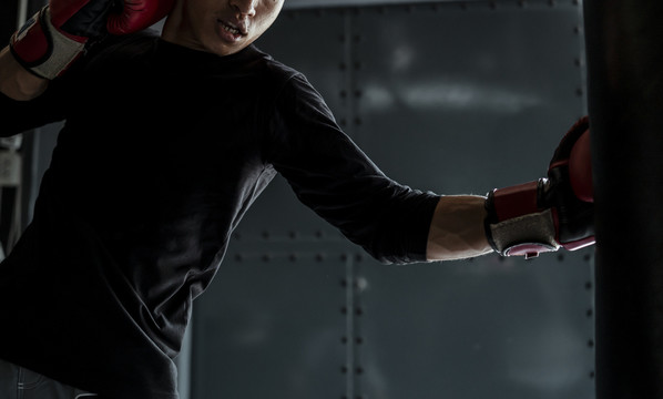 亚泰体育男子戴红手套打孔沙袋。在体育馆练习泰拳。