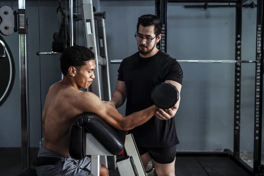侧视图-教练和运动员亚泰体育男子工作在杠铃长凳站在健身房。