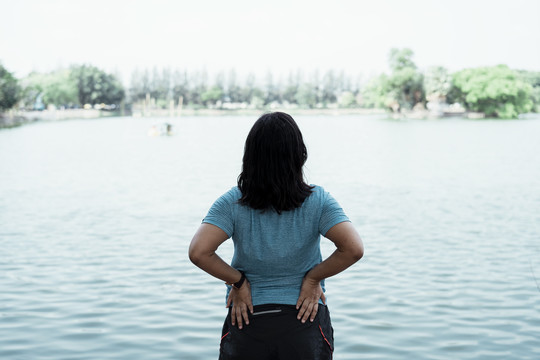 后视图-胖乎乎的亚洲女人在湖边伸展身体，在大自然中慢跑前热身。