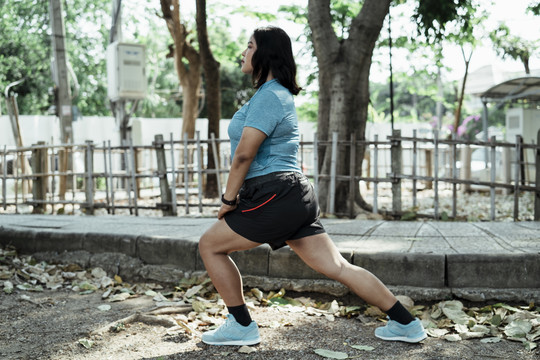 胖乎乎的亚洲女人在公园里跑步前伸腿。