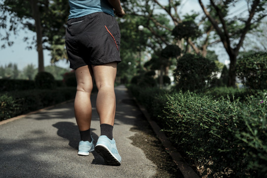 后视图-胖乎乎的运动型亚洲女子穿着蓝色运动服在公园跑道上慢跑。