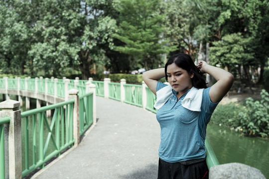 胖乎乎的运动型亚洲女子穿着蓝色运动服在公园跑步后放松。