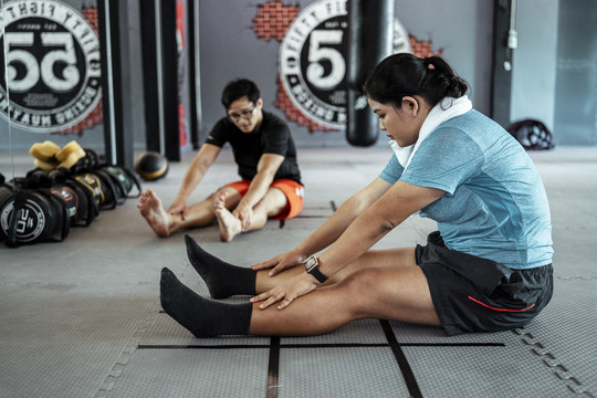 胖乎乎的运动型亚洲女性，穿着蓝色运动服，在健身房里伸展双腿。
