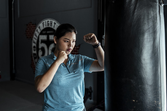 穿着蓝色运动服的亚洲胖女人在健身房练习带沙袋的泰拳。