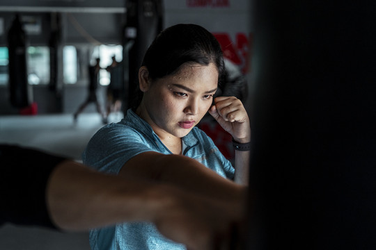 穿着蓝色运动服的亚洲胖女人在健身房练习带沙袋的泰拳。