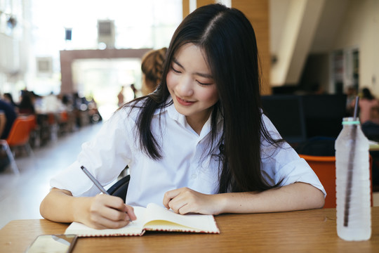 漂亮的黑发青年大学生在图书馆用钢笔在书页上统一书写。