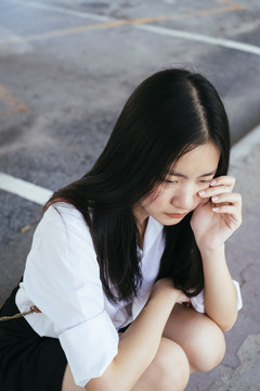 美丽的深色长发的特写写真身着校服的大学生在户外沮丧地哭泣。