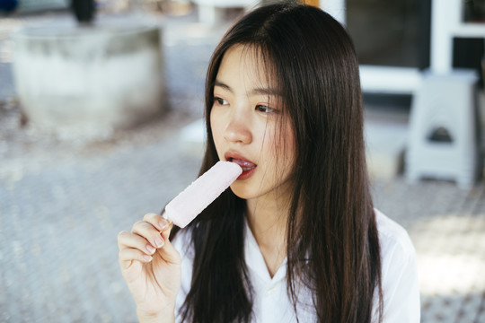 美丽的深色长发年轻大学生身着校服，喜欢在夏天吃冰激凌棒。