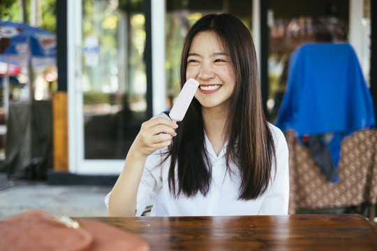 美丽的深色长发年轻大学生身着校服，喜欢在夏天吃冰激凌棒。