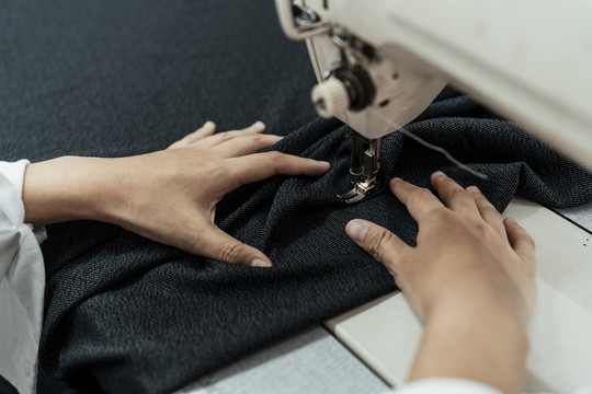 在工作台用缝纫机在黑布上工作的妇女的手。