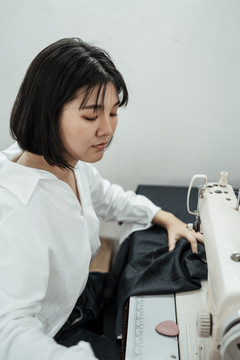 一位年轻的泰国女设计师，穿着黑布在缝纫站工作。
