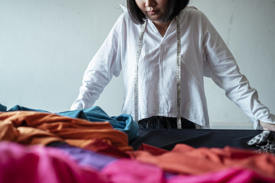 一位年轻的亚洲设计师，穿着白衬衫，看着她面前的彩色衣服。