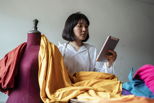 一位年轻的亚洲女设计师正在用五颜六色的生布做衣服。