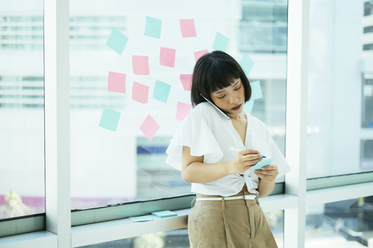 黑发女人站在办公室里，她接老板的电话，记下便条，然后贴在玻璃上。