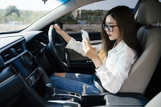 交通和车辆概念-泰国妇女戴着眼镜在开车时使用智能手机。