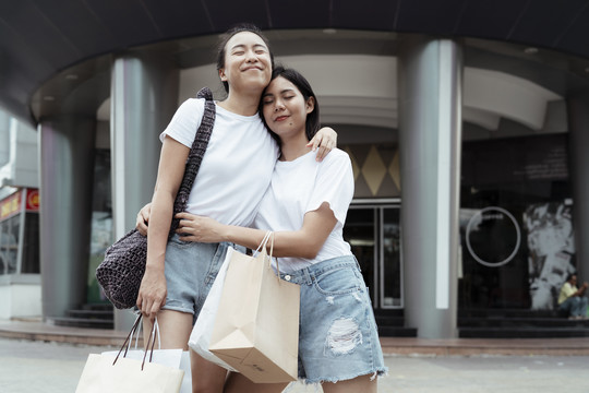 LGBTQ女同性恋者穿休闲装拥抱对方。两人都喜欢在购物中心购物。